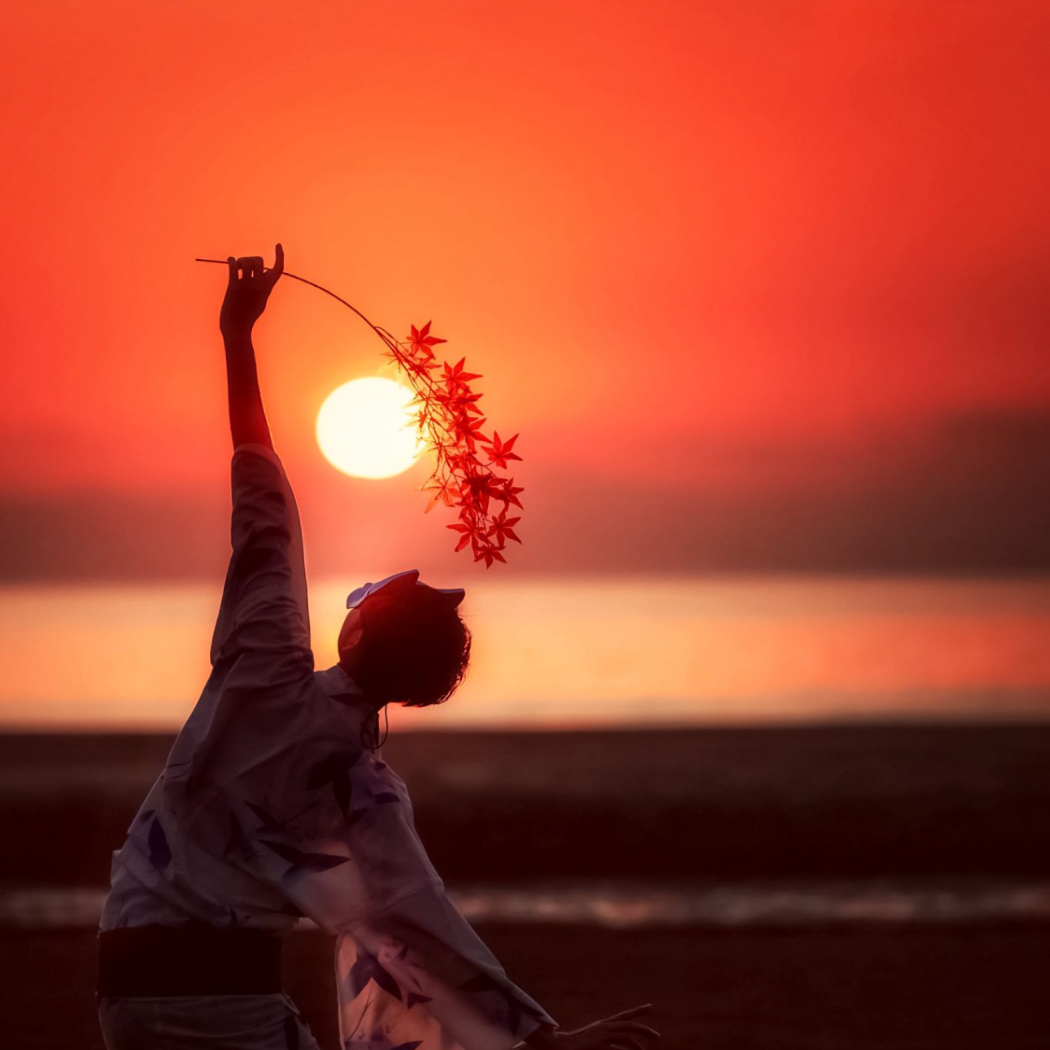 真っ赤な夕焼けに紅葉をかざした浴衣姿の写真